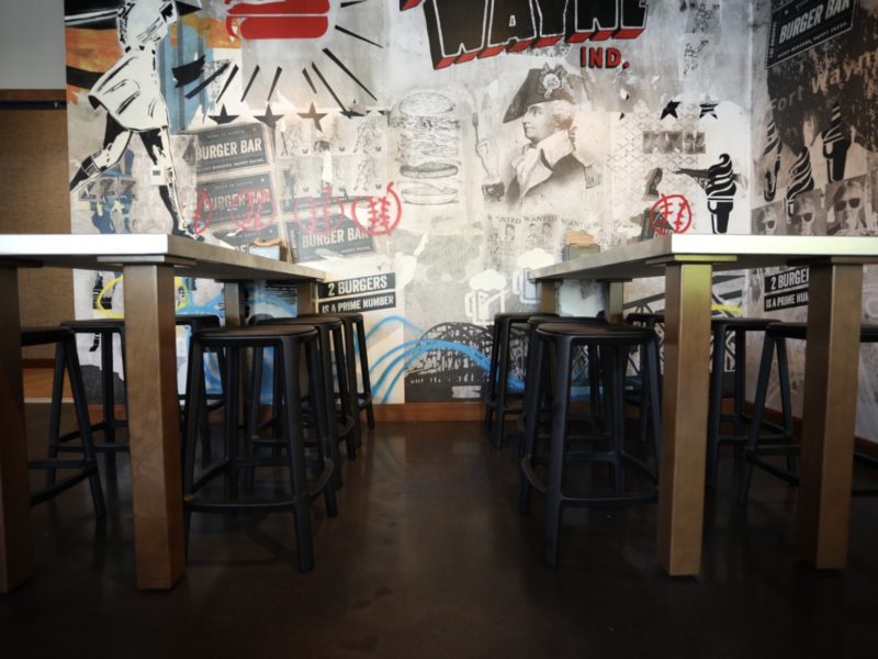 Tucked in stools under industrial tables in front of a busy wall