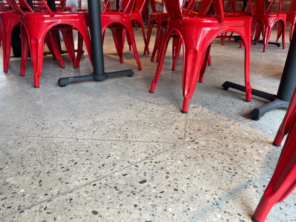 A polished concrete floor with a mix of small and large stones with saturated red dining chairs